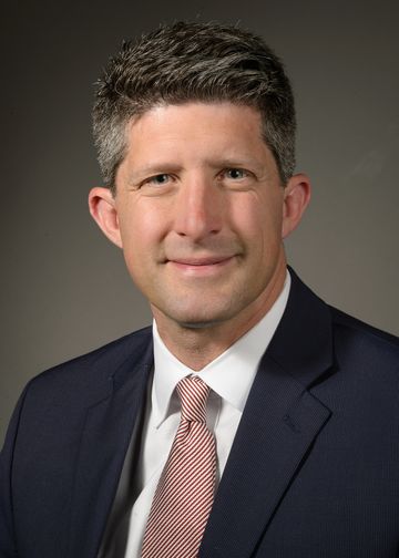 Joseph Schulman wearing a dark suit and red and white stripped tie